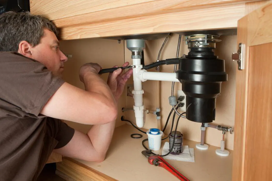 Plumber installing a new garbage disposal under a kitchen sink in Stark County, Ohio